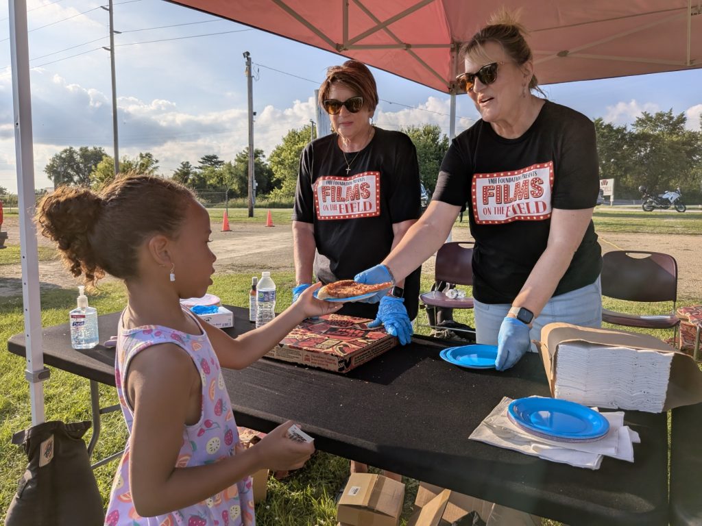 Image of films on a field volunteers handing out snacks to a child